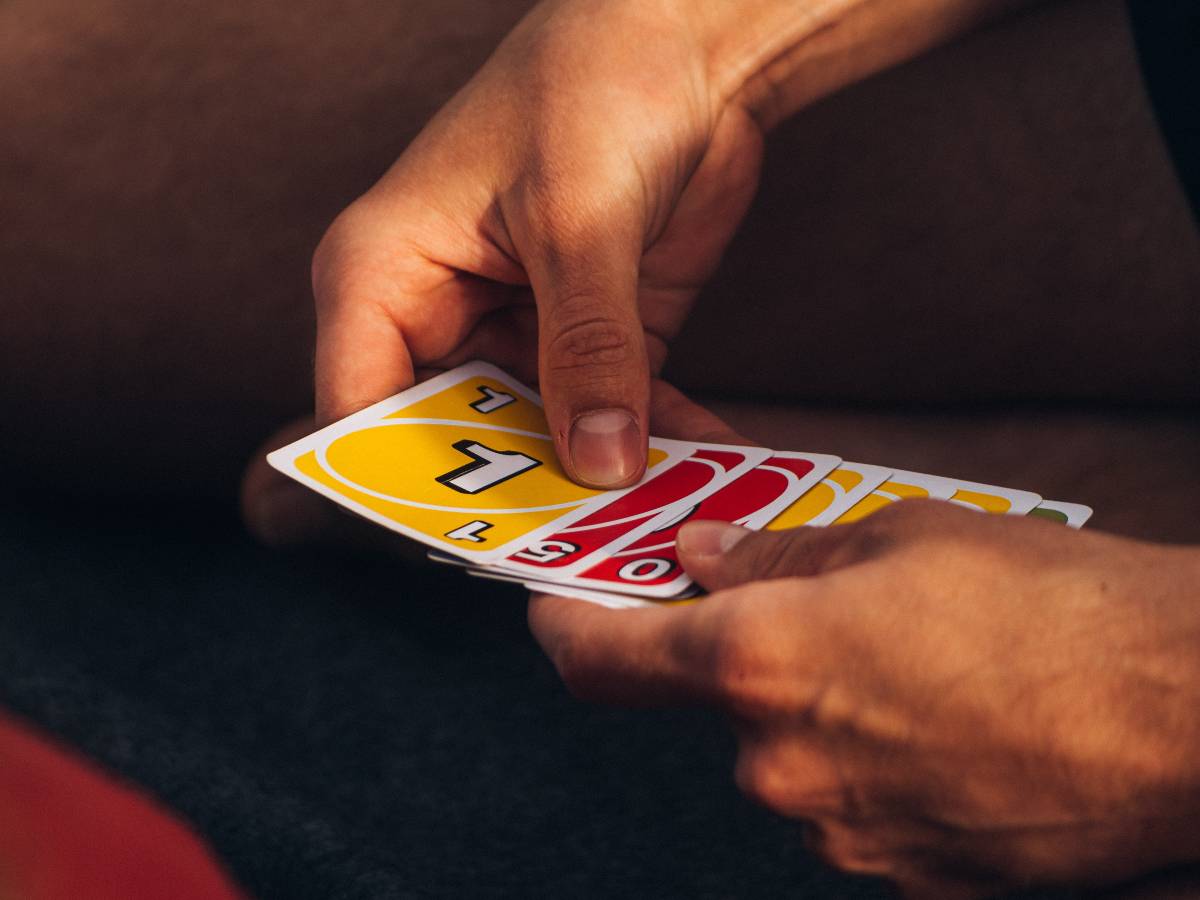 A pair of hands holding several Uno cards, a game that should be added to a list of camping must haves